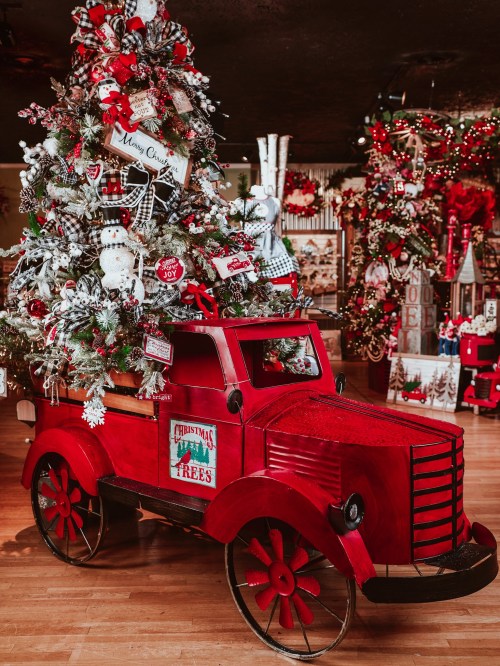 A vintage red truck adorned with a festive Christmas tree and holiday decorations, set in a cheerful holiday display.