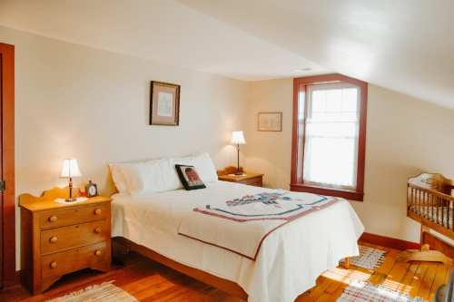 Cozy bedroom with a bed, nightstands, lamps, and a wooden crib, featuring warm lighting and rustic decor.