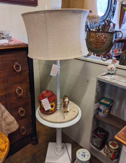 A vintage lamp with a fabric shade stands beside a decorative jar and a small figurine on a round table.