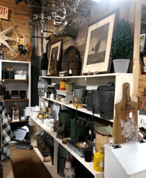 A vintage display featuring various antiques, decor items, and collectibles on white shelves in a rustic setting.