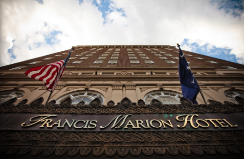 View of the Francis Marion Hotel from below, featuring American flags and a cloudy sky above.