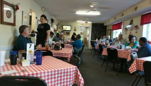 A cozy diner with checkered tablecloths, patrons dining, and a server taking an order at a table.
