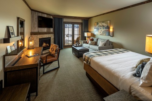Cozy hotel room featuring a bed, seating area, desk, fireplace, and large windows with a scenic view.