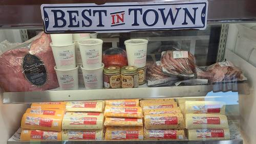 Display case featuring various meats, cheeses, and canned goods, labeled "Best in Town."