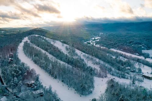 A snowy mountain landscape with ski trails, trees, and a sunset illuminating the scene.