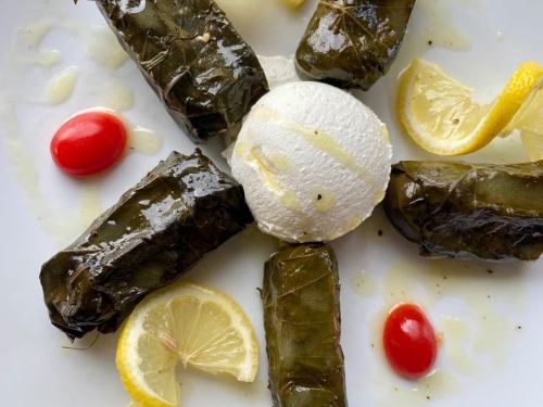 A plate of stuffed grape leaves arranged with lemon slices, cherry tomatoes, and a scoop of creamy white cheese.