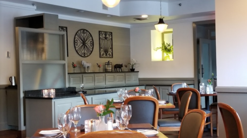 A cozy restaurant interior with wooden tables, elegant chairs, and decorative wall art. Soft lighting creates a warm ambiance.