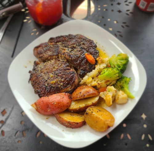 A plate of grilled steak with seasoned potatoes and a mix of broccoli, cauliflower, and carrots.