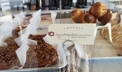 A display case with various baked goods, including a pecan sticky bun priced at $3.50.