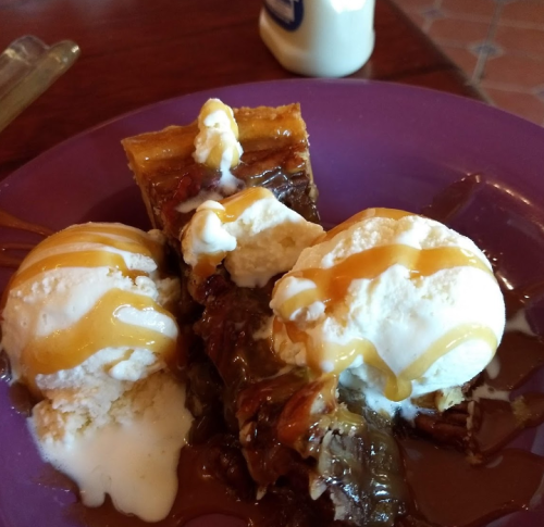A purple plate with a slice of pie topped with two scoops of ice cream drizzled with caramel sauce.