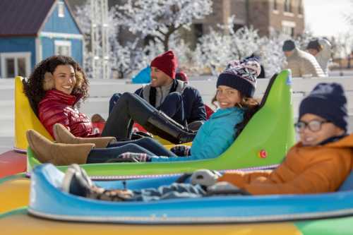 A group of friends enjoying a winter day on colorful snow tubes, smiling and dressed in warm jackets and hats.