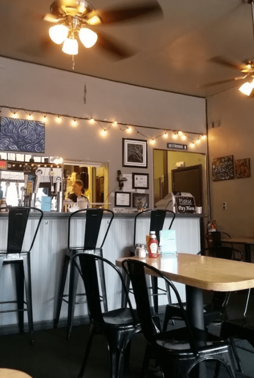 Cozy café interior with black chairs, a counter, string lights, and a restroom sign in the background.