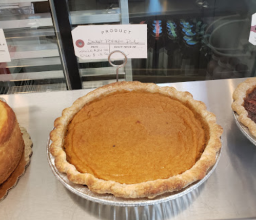 A freshly baked sweet potato pie in a silver pie dish, displayed alongside other desserts in a bakery.