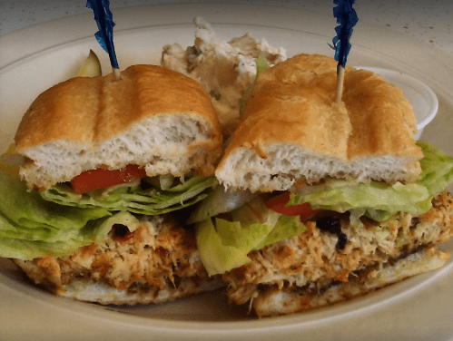 A close-up of a sandwich with shredded chicken, lettuce, and tomato, served with a side of potato salad.