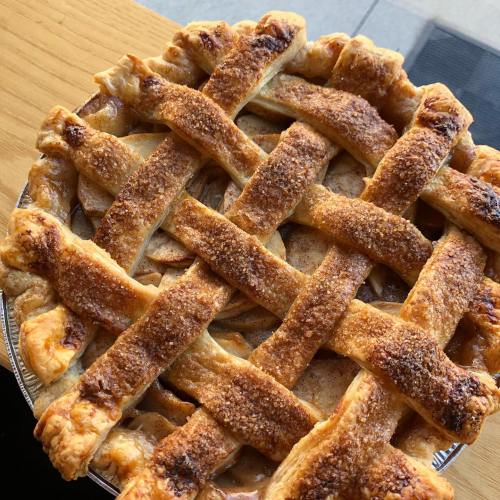 A freshly baked apple pie with a golden, lattice crust and a sprinkle of sugar on top, resting on a wooden surface.