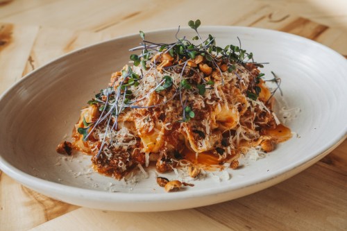A plate of pasta topped with herbs, cheese, and nuts, served on a wooden table.
