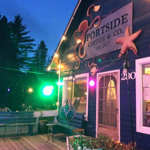 A cozy coffee shop exterior at dusk, featuring colorful lights and a sign that reads "Portside Coffee & Co."