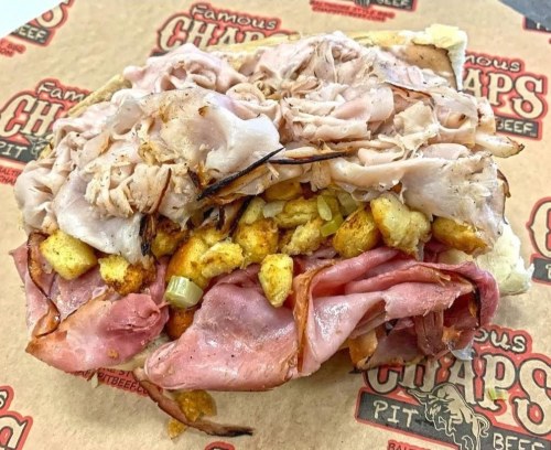 A hearty sandwich piled high with layers of turkey, ham, and stuffing on a soft roll, served on butcher paper.