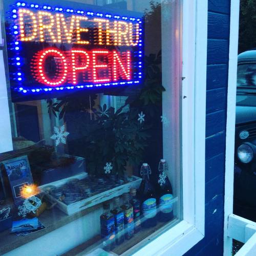 Bright neon "OPEN" sign in a window, with a "DRIVE THRU" message and various bottles displayed inside.