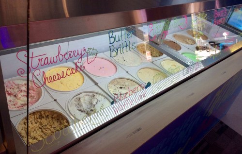 A display of various ice cream flavors in a glass case, with colorful labels for each flavor.
