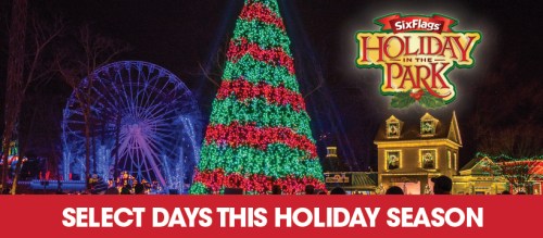 Colorful holiday lights decorate a large tree and buildings at Six Flags, with a Ferris wheel in the background.