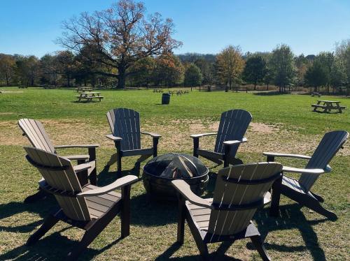 A circle of wooden chairs around a fire pit in a grassy park with trees and picnic tables in the background.