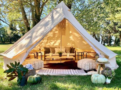 A cozy glamping tent with seating, cushions, and decor, set in a sunny outdoor space surrounded by trees.