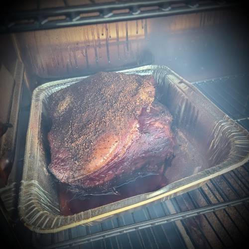 A smoked brisket in a foil pan, resting in a smoker with steam and smoke surrounding it.