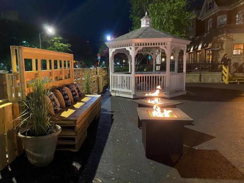 A cozy outdoor space at night featuring a gazebo, seating area, and a fire pit surrounded by greenery.