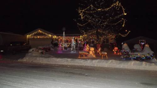 A snowy house decorated with colorful Christmas lights and festive displays, including reindeer and a snowman.