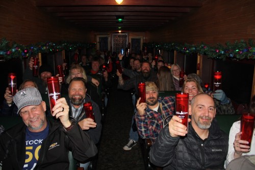 A group of people inside a decorated train car, smiling and raising red cups in celebration.