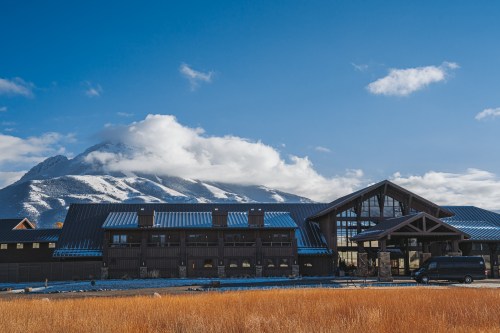 A modern building with a blue roof, set against a backdrop of snow-capped mountains and a clear blue sky.