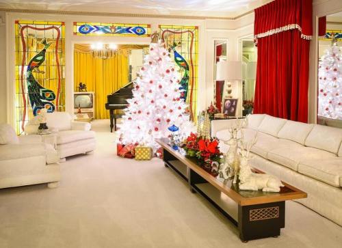 A festive living room with a white Christmas tree, red curtains, and a piano, decorated for the holidays.