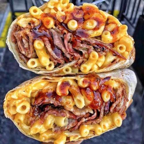 A close-up of a burrito filled with macaroni and cheese, pulled pork, and barbecue sauce, cut in half to show the filling.