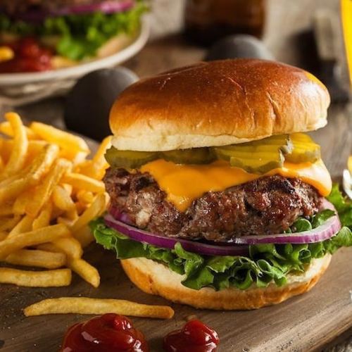 A juicy cheeseburger with lettuce, pickles, and onions, served with crispy fries and ketchup on a wooden table.