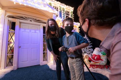 A woman and a child in masks stand in front of a festive, decorated doorway, while another person looks on.