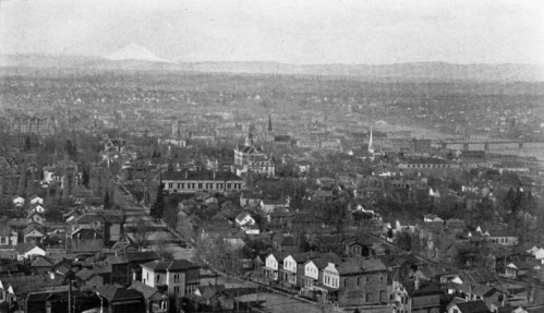 A historic black-and-white aerial view of a cityscape with houses, churches, and distant mountains.