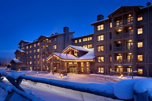 A cozy lodge illuminated at dusk, surrounded by snow, with warm lights glowing from the windows.