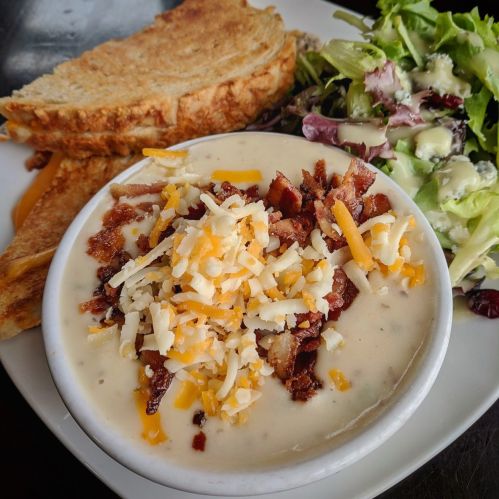 A bowl of creamy soup topped with bacon and cheese, served with toasted bread and a side salad.