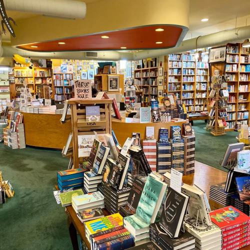 A cozy bookstore filled with shelves of books, tables stacked with titles, and a welcoming atmosphere.