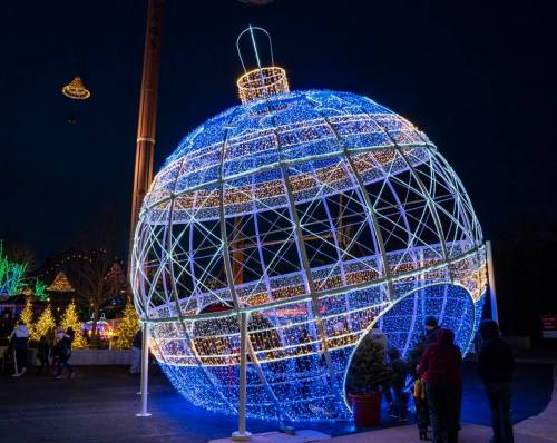 A large illuminated ornament structure with blue and white lights, surrounded by festive decorations and people at night.