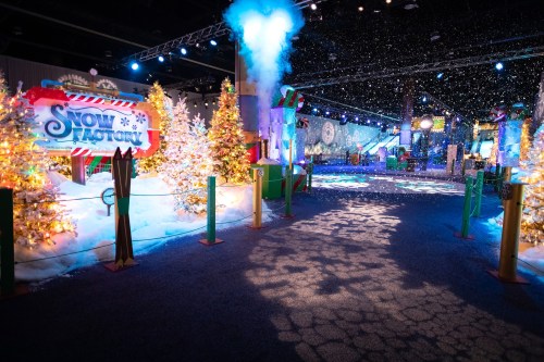 A festive indoor scene with snow, decorated trees, and colorful lights, featuring a "Snow Factory" sign.