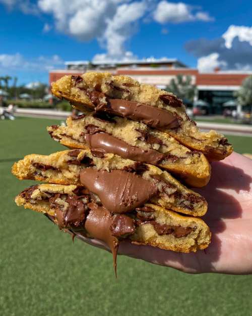 A hand holding a stack of warm, gooey chocolate chip cookies filled with melted chocolate.