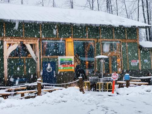 A cozy green building covered in snow, with heavy snowfall and outdoor seating visible.