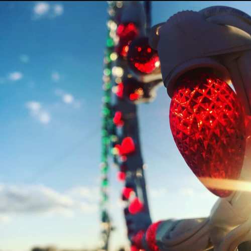 Close-up of colorful holiday lights against a bright blue sky with clouds.