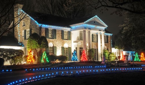 A beautifully lit stone house at night, adorned with colorful Christmas lights and festive trees in the yard.