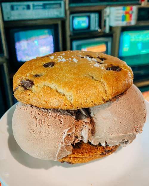 A chocolate chip cookie sandwich filled with chocolate ice cream, set against a backdrop of vintage televisions.