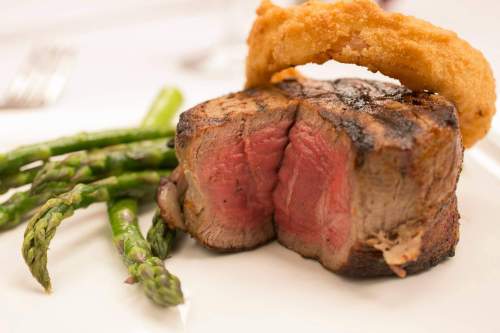 A perfectly cooked steak with a crispy onion ring, served alongside fresh asparagus on a white plate.