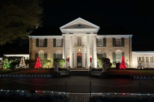 A beautifully lit mansion decorated for the holidays, featuring colorful lights and festive trees in the front yard.