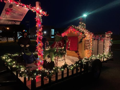A festive trailer decorated with lights, featuring holiday figures and a small cabin, set against a night sky.